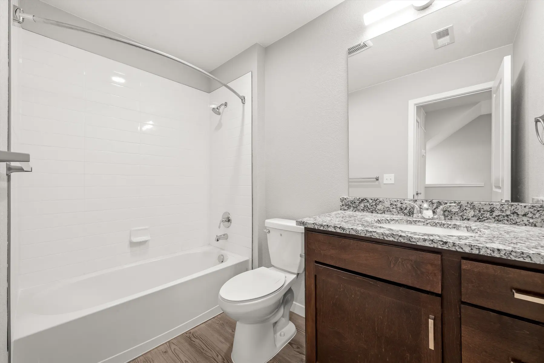 Modern Bathroom Design A modern bathroom featuring a bathtub with a shower, a toilet, and a granite countertop vanity. The walls are painted in a light gray color, and the floor has a wood-like finish.