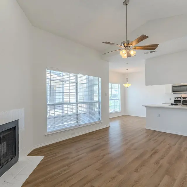 Spacious living room featuring a white wall, large windows with blinds, a ceiling fan, and a fireplace.