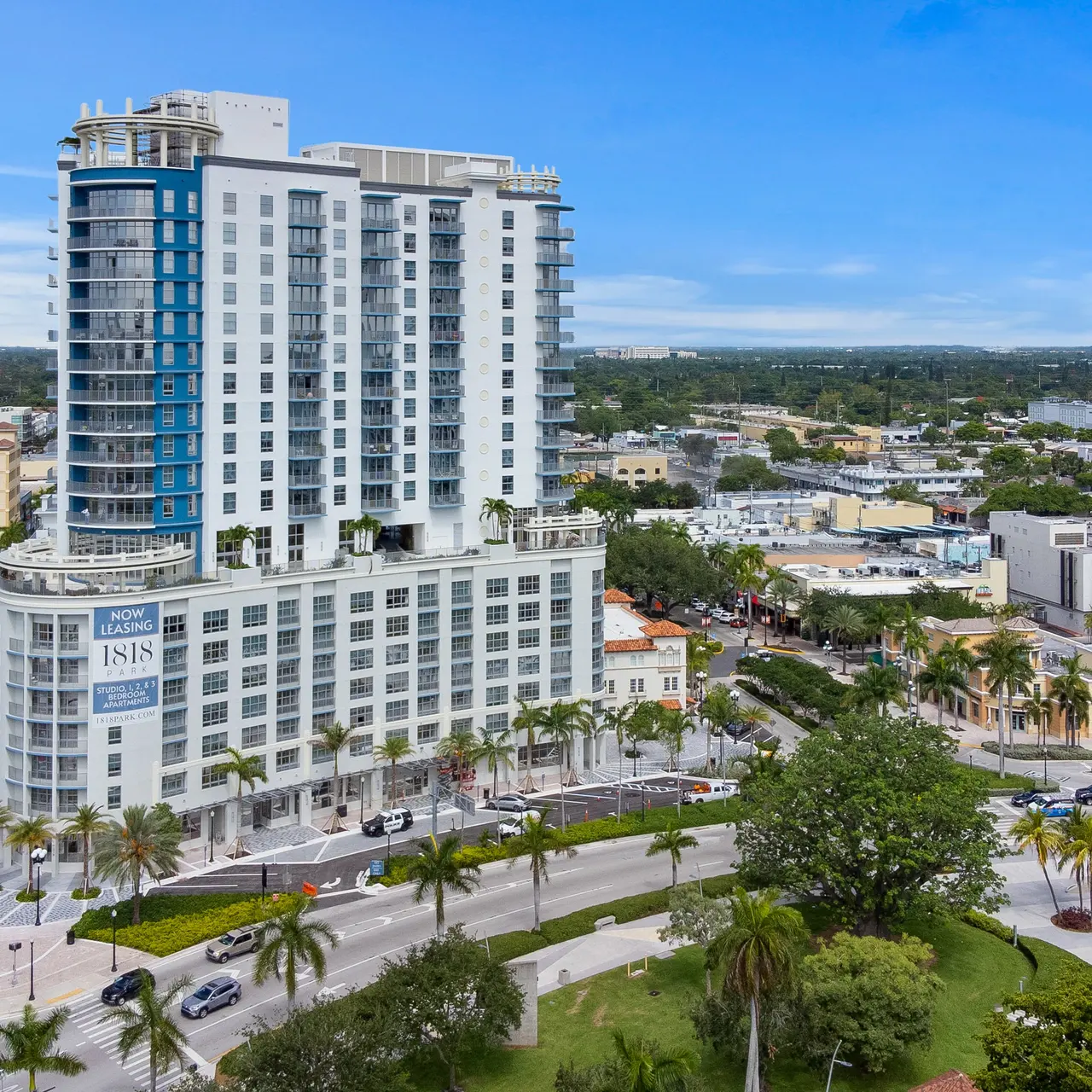 A modern high-rise apartment building surrounded by palm trees and city streets.