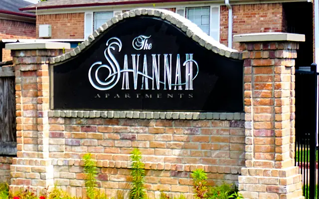 Sign for The Savannah Apartments, featuring a brick base and an arching black panel with elegant white lettering.