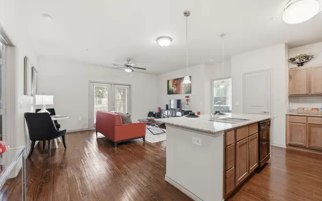 A spacious and modern apartment interior featuring a living area with a red sofa, a dining area, and a kitchen with wooden cabinets and a granite island.