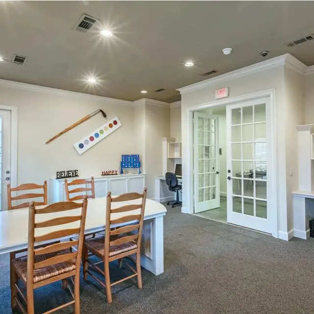 Modern Office Space An office space with a central white table surrounded by wooden chairs, shelves on the side with decorative items, and a glass door leading to another room.