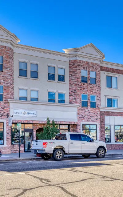 A modern commercial building with a mix of brick and stucco facade, featuring several businesses on the ground floor. The structure has three stories with large windows and a clear blue sky overhead.