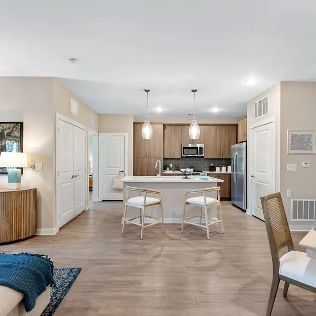 Modern Apartment Interior A modern apartment interior featuring a spacious living room and kitchen area. The decor includes a beige color palette, stylish pendant lights, and wooden flooring. There are seating arrangements at a dining table and kitchen island, with decorative elements like vases and a cozy throw blanket.