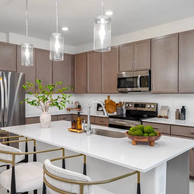 A modern kitchen featuring a large island with bar stools, stainless steel appliances, and wood cabinetry.