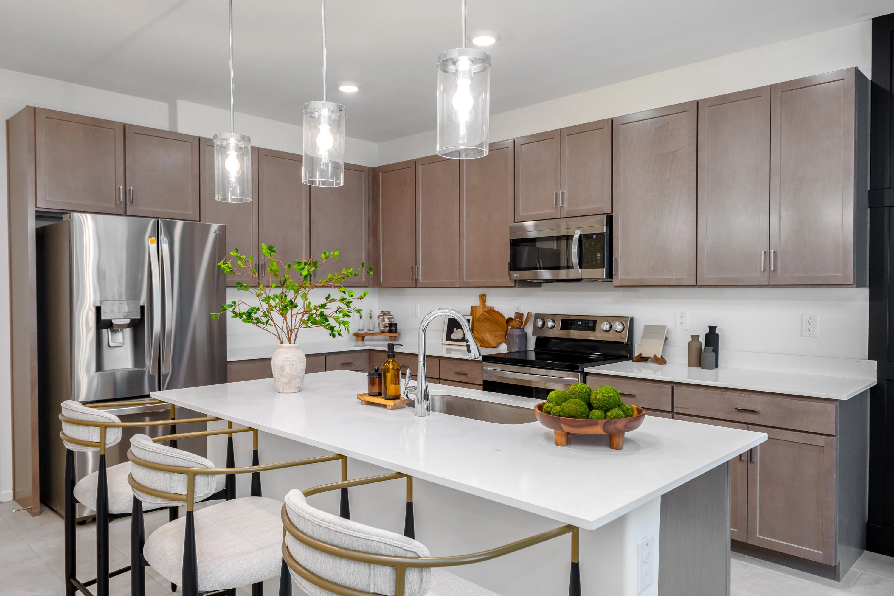 A modern kitchen featuring a large island with bar stools, stainless steel appliances, and wood cabinetry.