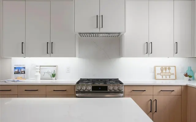 A modern kitchen featuring a combination of light and dark cabinetry, a stainless steel stove, and white marble countertops with subtle lighting under the cabinets.