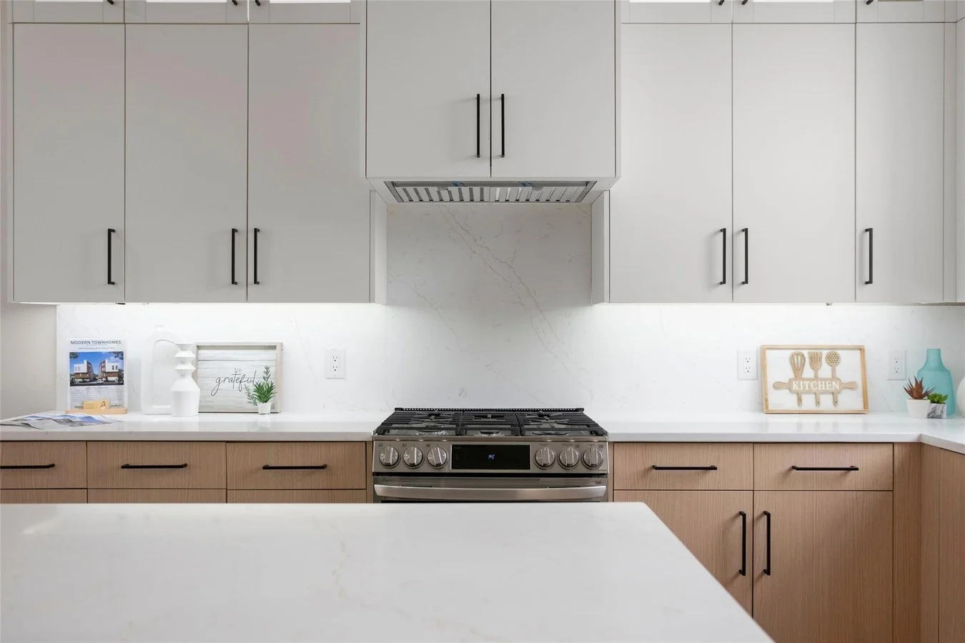 A modern kitchen featuring a combination of light and dark cabinetry, a stainless steel stove, and white marble countertops with subtle lighting under the cabinets.