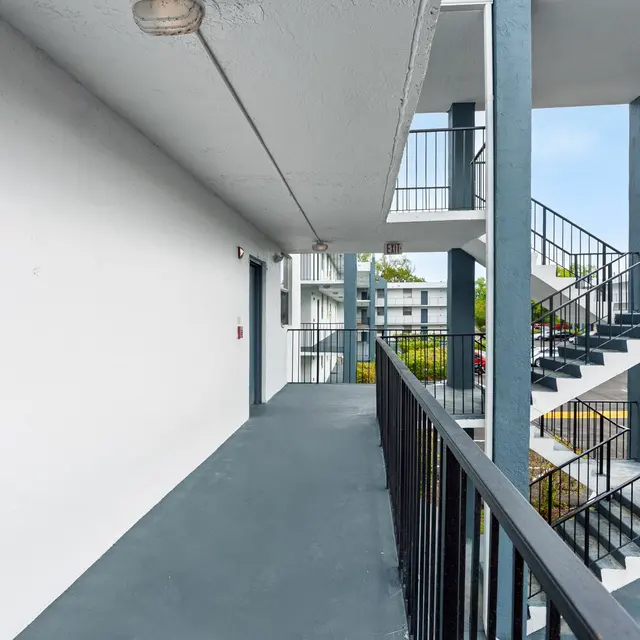 A view of a modern apartment complex's exterior walkway and staircases, featuring gray concrete floors and blue pillars.