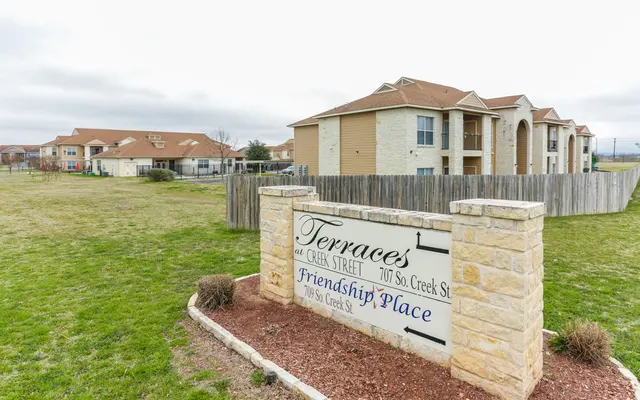 Sign for Terraces and Friendship Place apartment community, featuring a landscaped area and nearby buildings.
