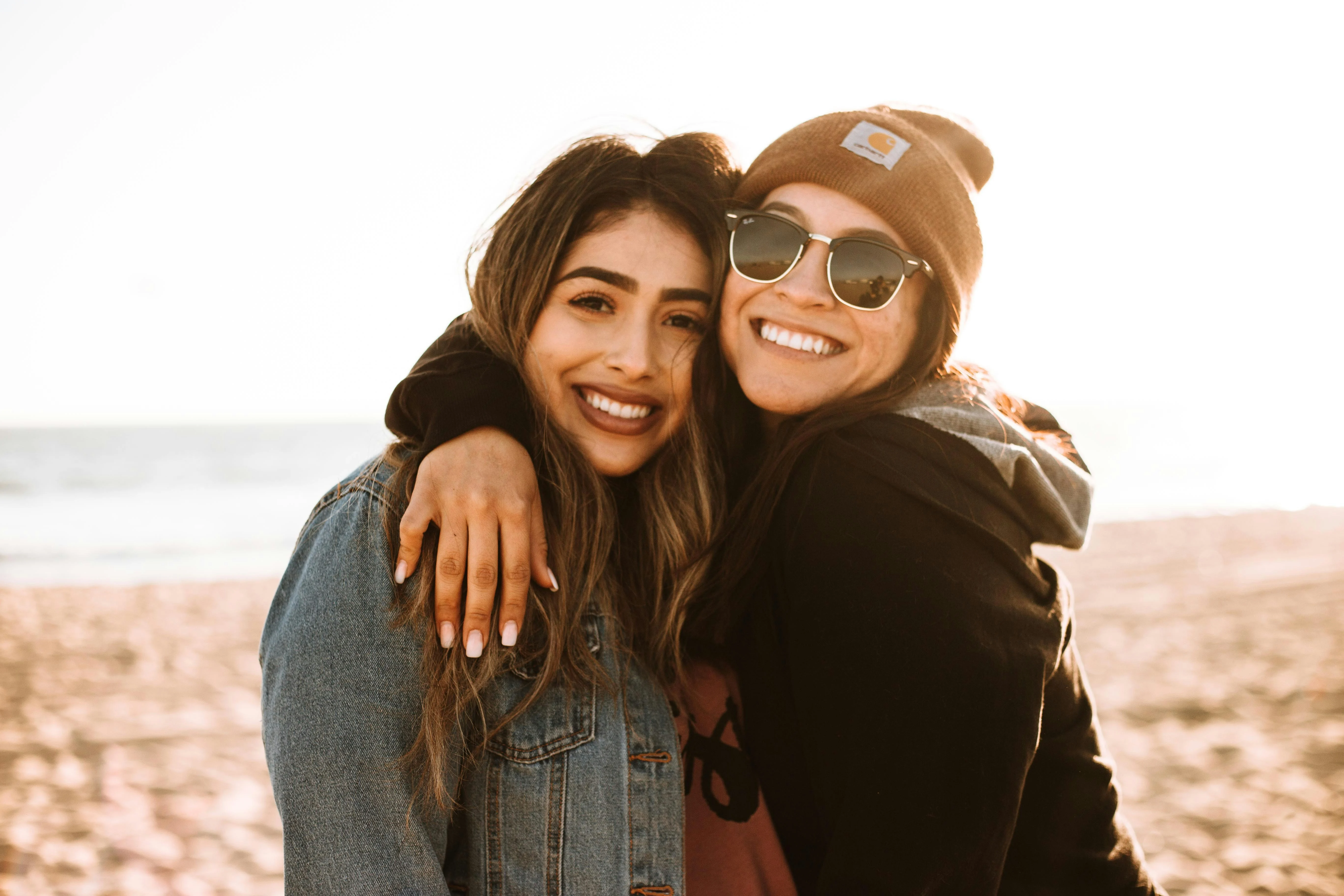 Friends Enjoying a Sunset at the Beach Two friends smiling and embracing each other at the beach during sunset.