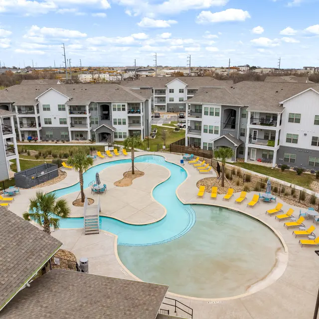Aerial view of a modern apartment complex featuring a pool shaped like a lagoon surrounded by lounge chairs.