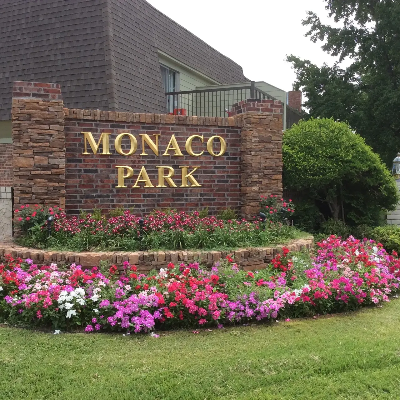 A brick sign reading 'Monaco Park' surrounded by colorful flower beds and greenery.