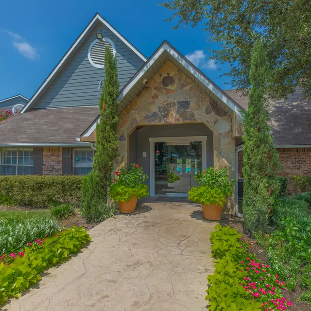 A charming house with a stone entryway surrounded by lush greenery and colorful flowers.