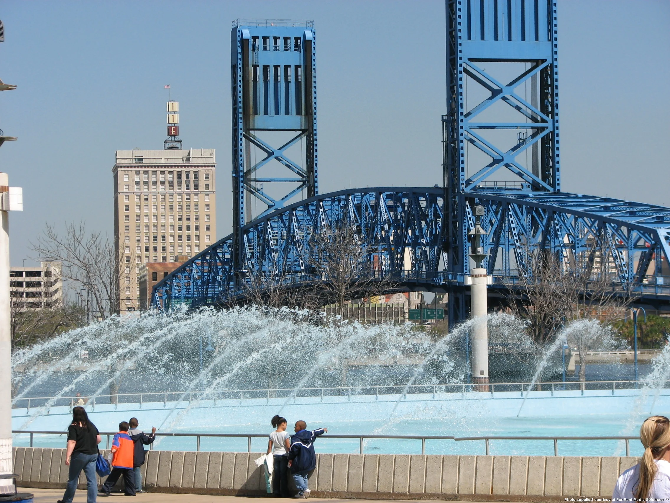 Blue Bridge and Fountain A blue bridge over a water fountain with people gathered nearby.