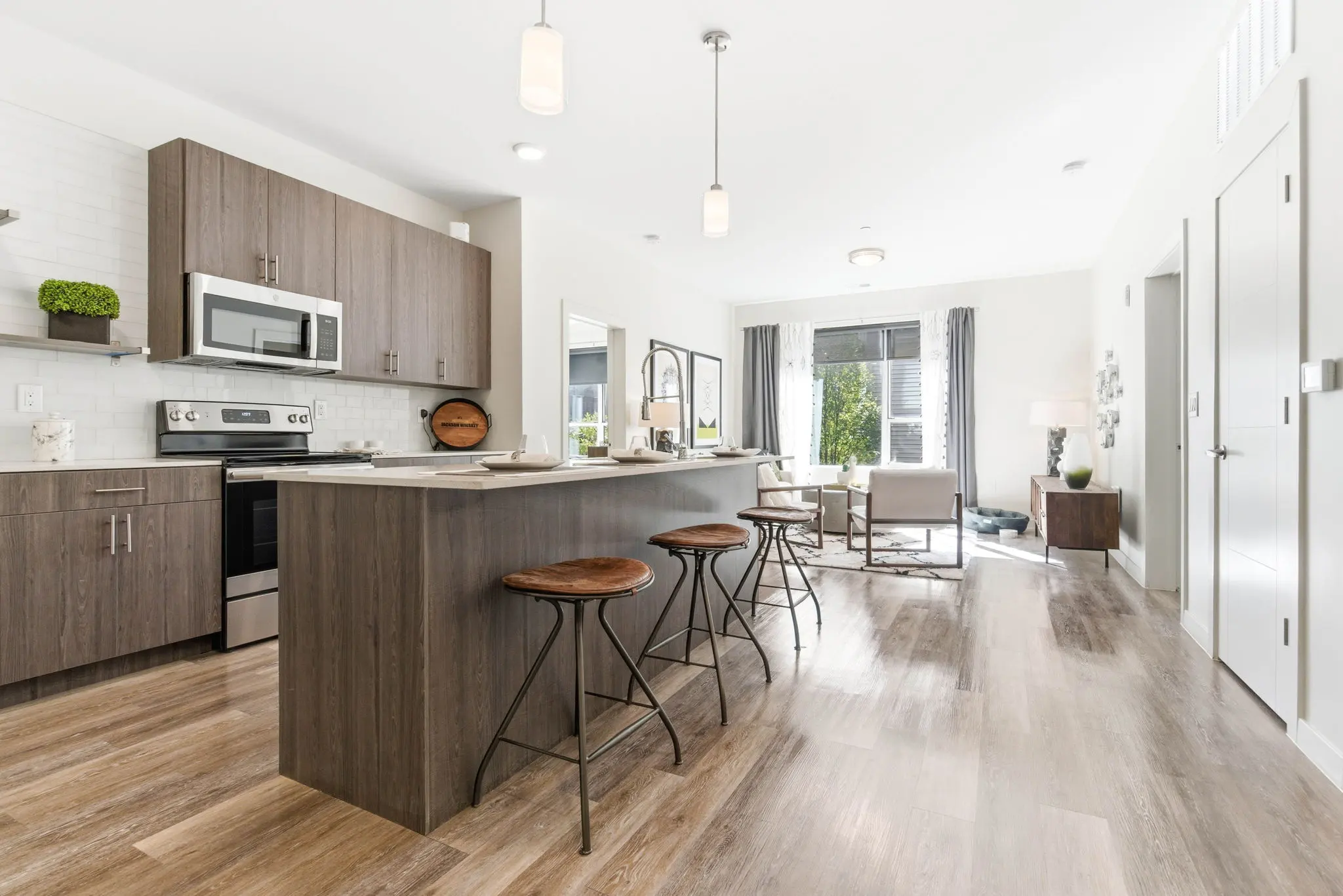 A contemporary kitchen with an island, stainless steel appliances, and a spacious living area in the background.