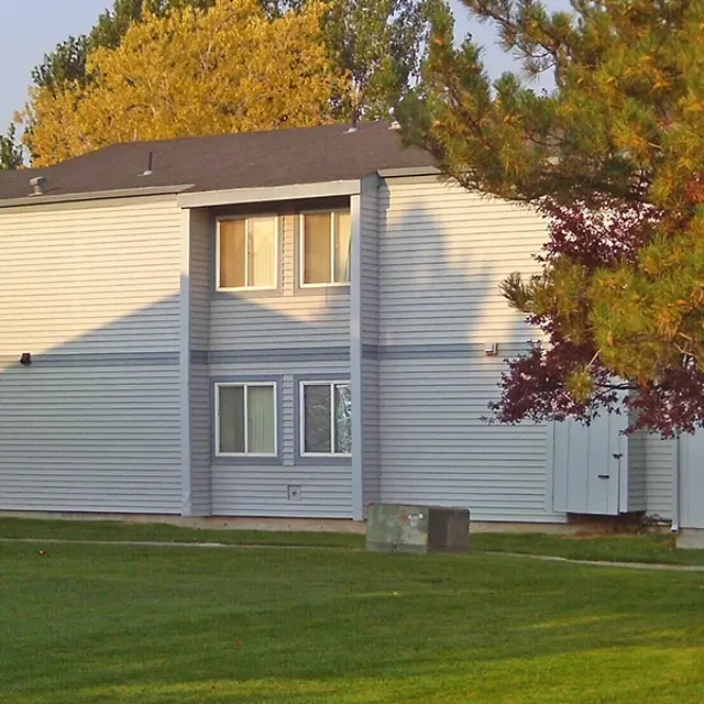 Exterior View of Apartment Building Exterior view of a two-story apartment building with grey siding and trees nearby.