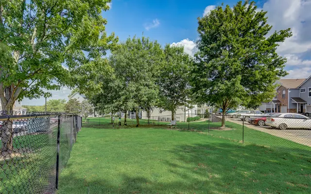 A green lawn area surrounded by trees and a fence, with residential buildings in the background.