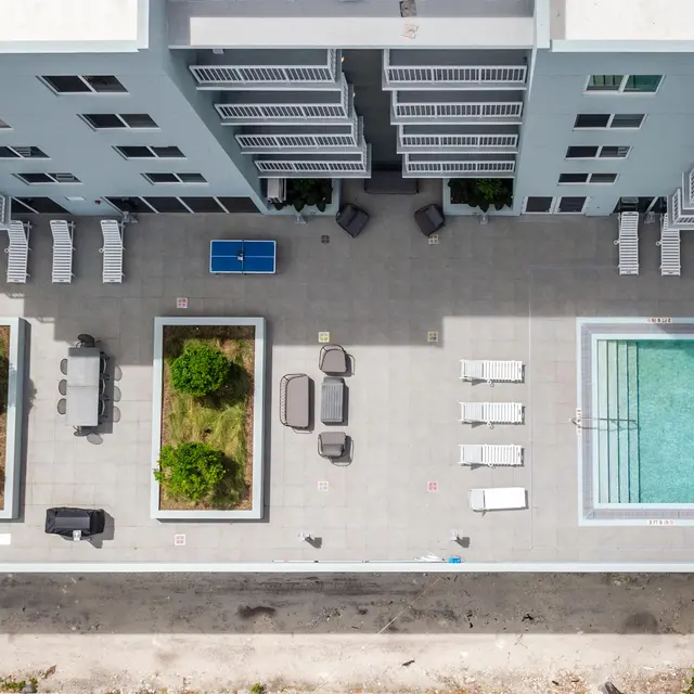 Aerial view of a modern apartment complex featuring a swimming pool, lounge chairs, and landscaped greenery.