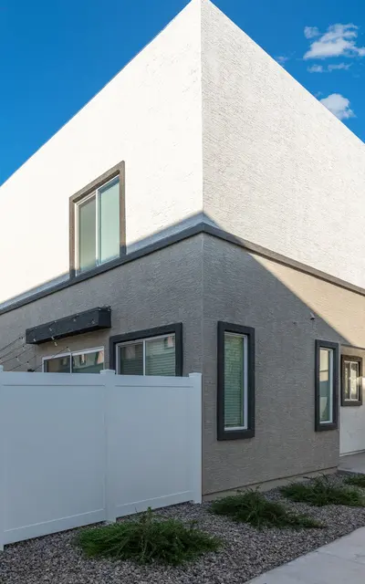 Contemporary House Design Contemporary exterior view of a two-story house with white walls and a gray section, surrounded by a white fence and landscaped pathways.
