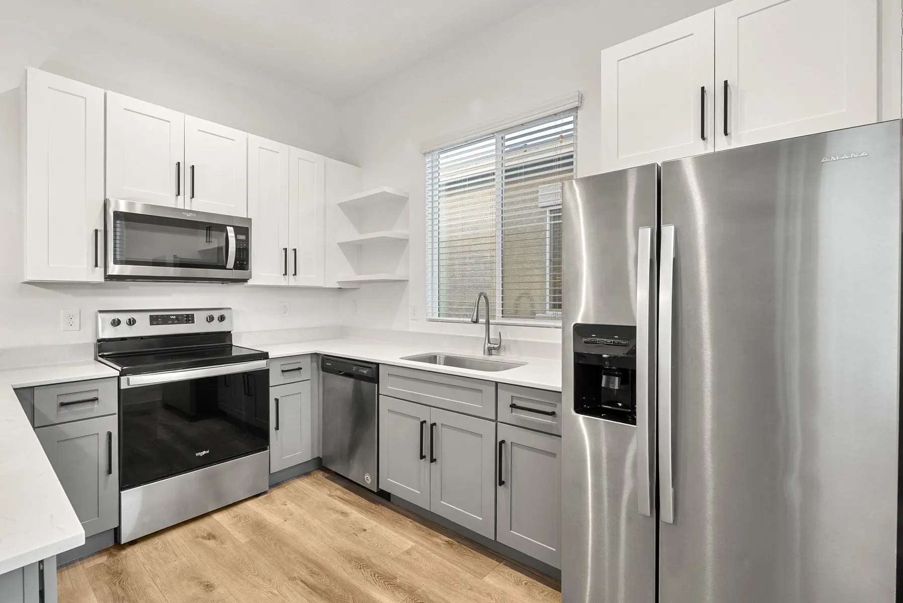 Modern kitchen featuring stainless steel appliances, gray and white cabinets, a sink, and a window for natural light.