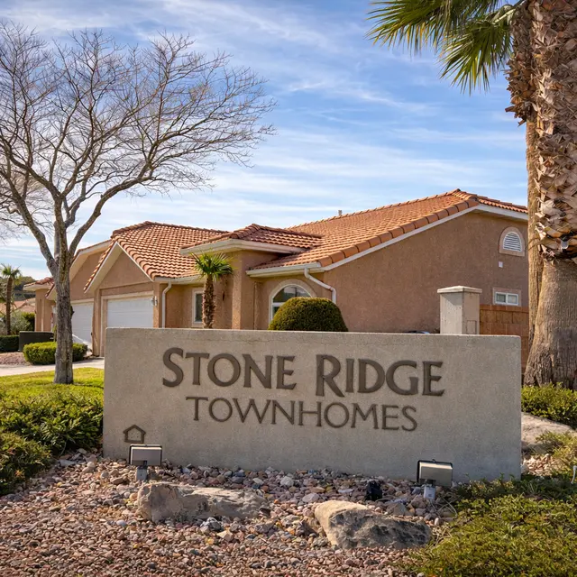 Sign indicating Stone Ridge Townhomes with a residential building in the background and palm trees nearby.