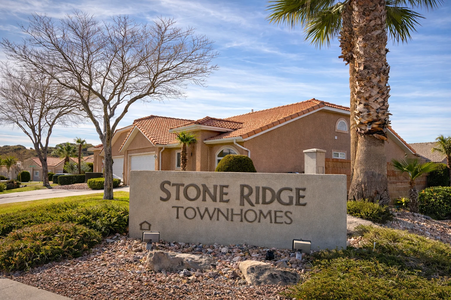 Sign indicating Stone Ridge Townhomes with a residential building in the background and palm trees nearby.