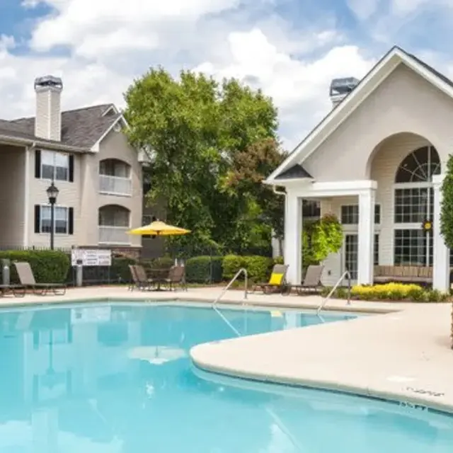 A tranquil apartment pool area featuring a clear blue swimming pool surrounded by lounge chairs and a poolside gazebo.
