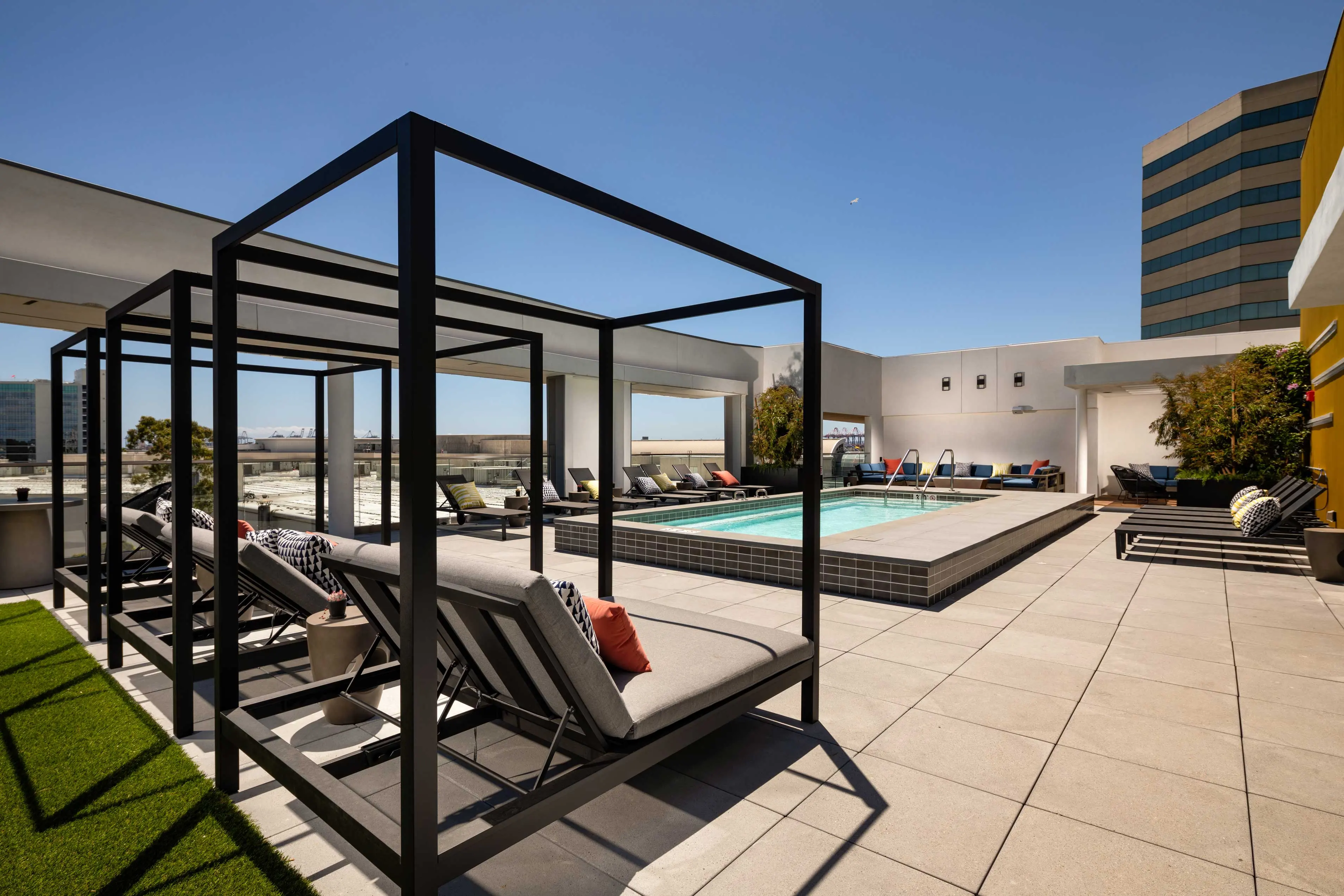 A modern rooftop pool area featuring lounge chairs and cabanas, with a beautiful blue sky above.