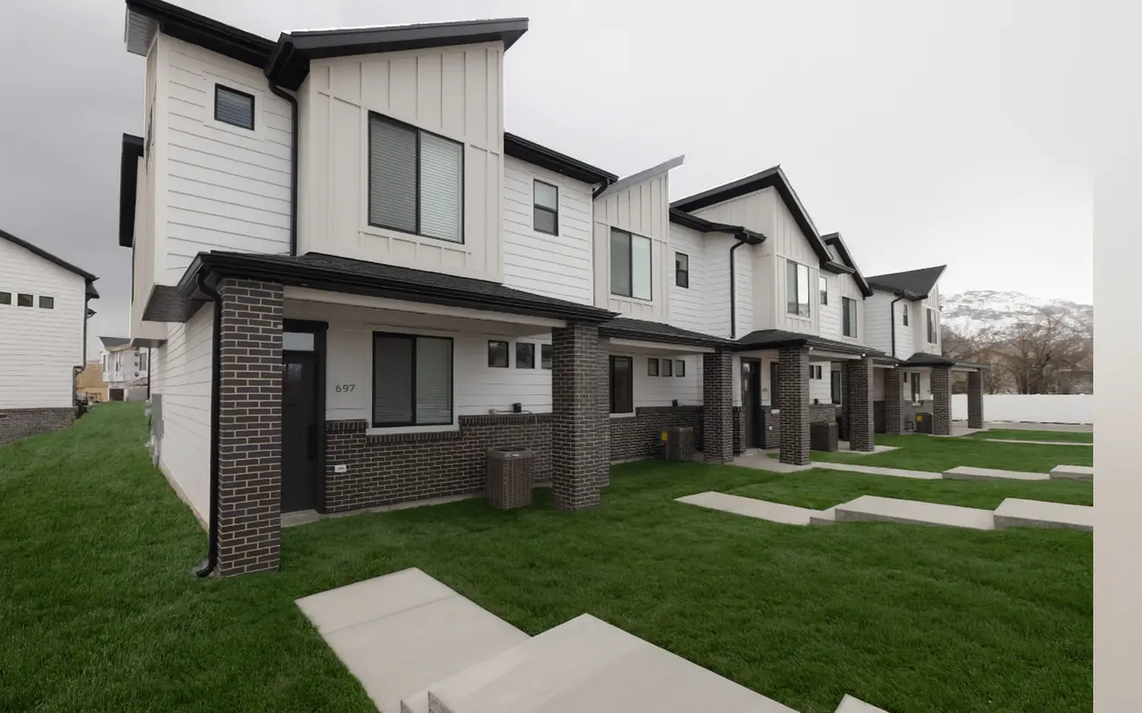 A row of modern two-story townhouses with a mix of white and black exteriors, situated in a neighborhood with green grass and concrete pathways.