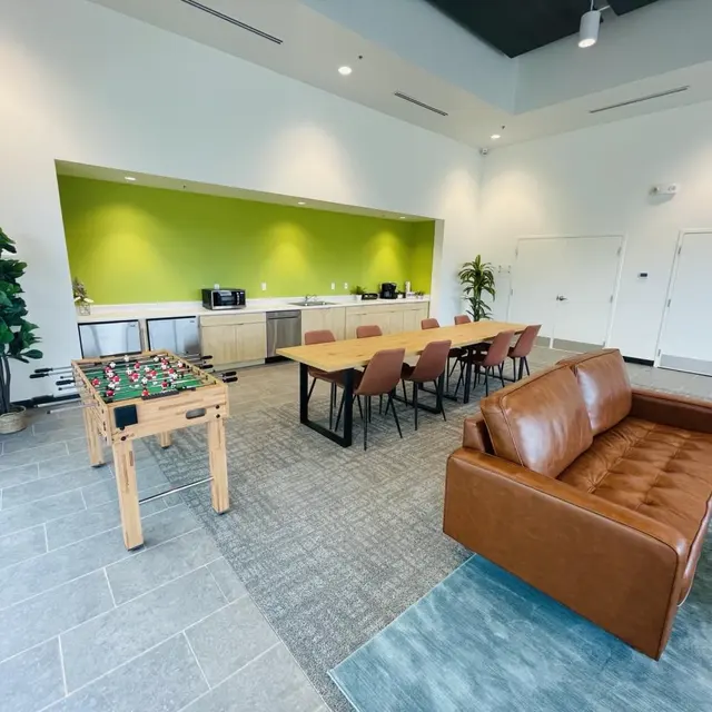 Modern Common Area A modern common area featuring a foosball table, a dining table with chairs, a brown sofa, and a kitchenette with green accent wall.