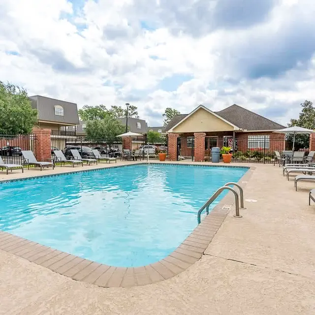 Clear swimming pool surrounded by lounge chairs and a clubhouse in the background.
