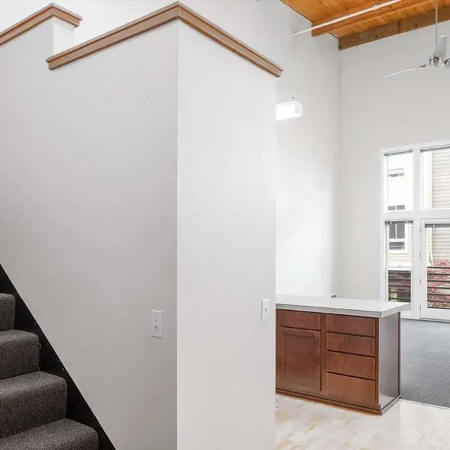 Interior view of a modern home showing a staircase and an open living area with large windows.