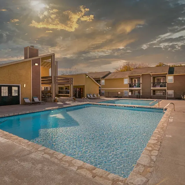 Apartment Pool Area A swimming pool surrounded by lounge chairs at an apartment complex, with buildings in the background under a cloudy sky.