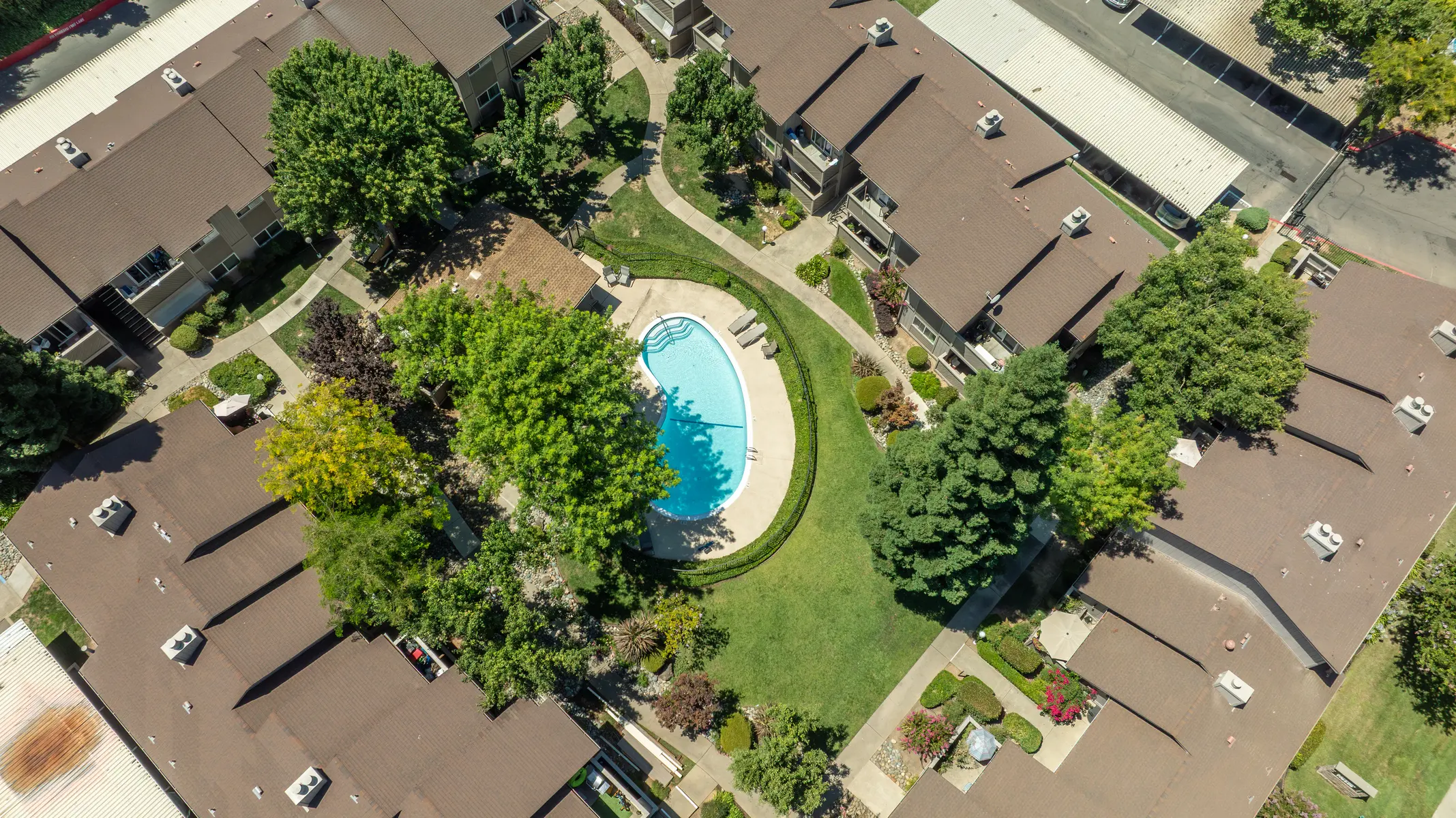 Aerial view of an apartment complex featuring a central swimming pool surrounded by green lawns and trees.
