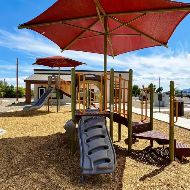 Playground with Shade Canopies A playground featuring multiple play structures with slides, shaded by large red canopies, surrounded by a sandy area.