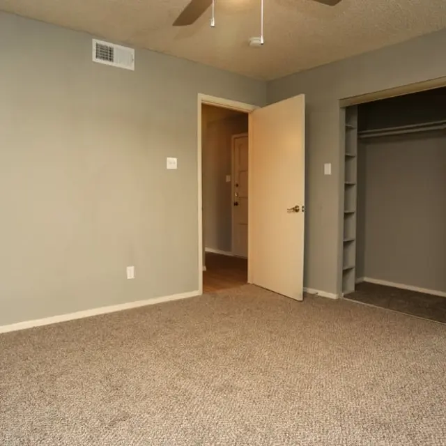 A vacant room with gray walls, a ceiling fan, and a mirrored closet door. The entrance is visible with an open door leading to another space.