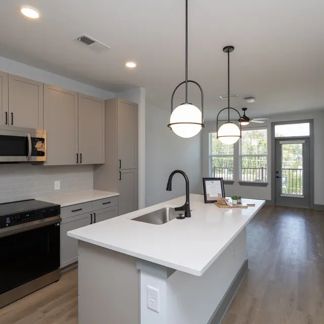 Modern kitchen with gray cabinets and a white countertop, featuring stainless steel appliances and pendant lighting.
