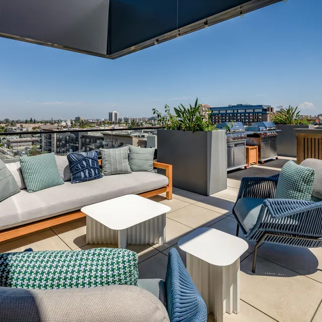 Modern Rooftop Lounge with City Views A modern rooftop lounge area featuring comfortable seating with cushions, small tables, and a view of a city skyline on a clear day.