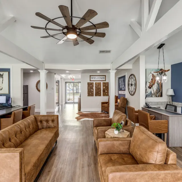 A modern lobby interior featuring comfortable brown couches, a large ceiling fan, and a welcoming atmosphere with decorative animal artwork on the walls.
