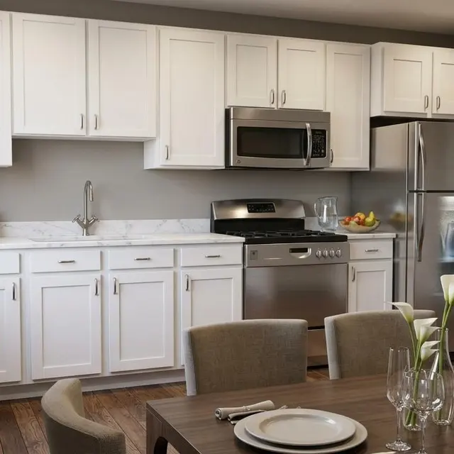 A modern kitchen and dining area featuring white cabinets, stainless steel appliances, and a wooden dining table with plates and glassware set.