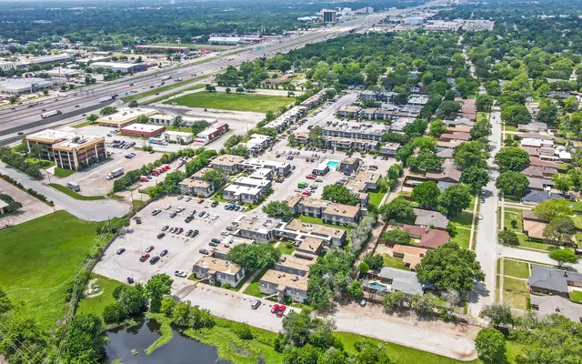 Aerial view of a suburban area featuring a mix of commercial and residential buildings, roads, and lush greenery.