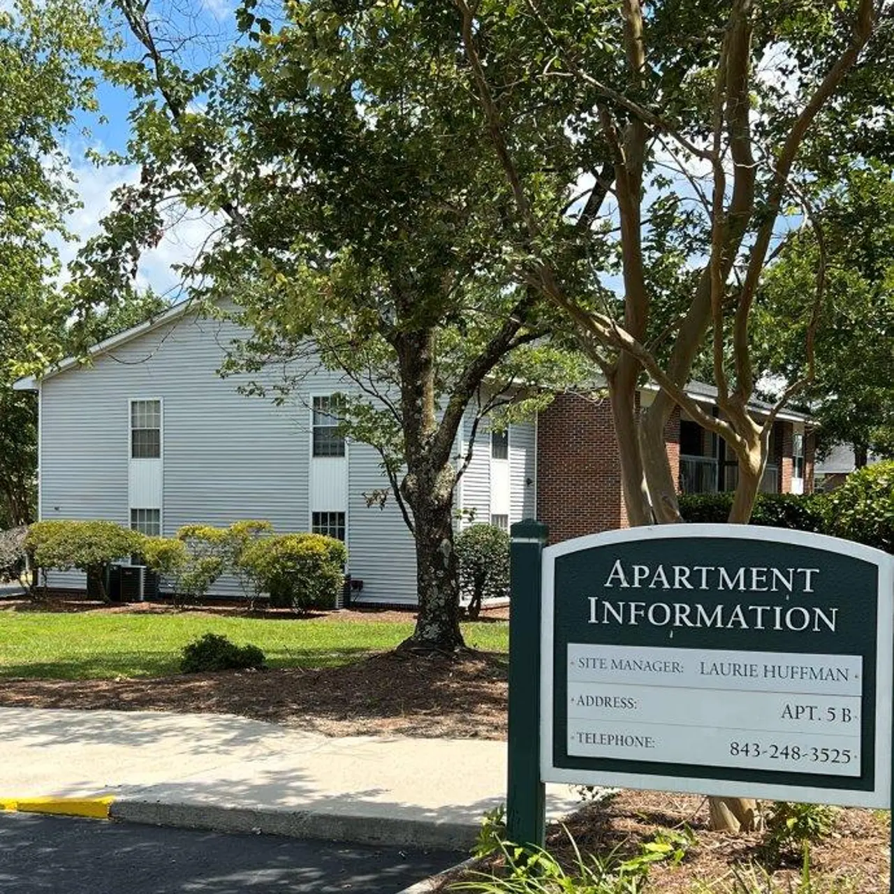 Sign indicating apartment information with site manager details in a residential area surrounded by greenery.