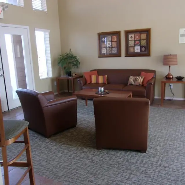 Cozy Living Room Interior A cozy living room with two brown armchairs and a brown couch, a coffee table in the center, and a small lamp on a side table. There are decorative frames on the wall and a plant in the corner. Natural light is coming through a door with windows.