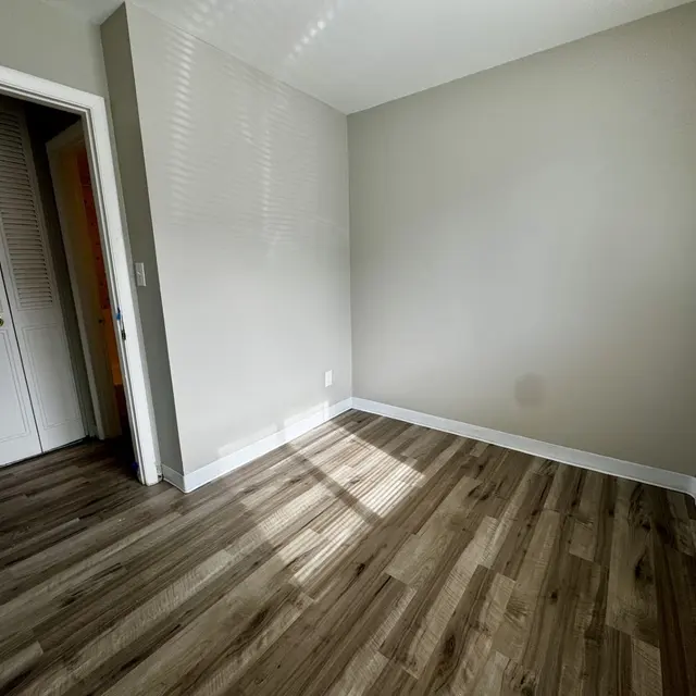 Empty Room with Natural Light An empty room with light-colored walls and wood-like flooring, featuring a door leading to a closet and a window letting in natural light.