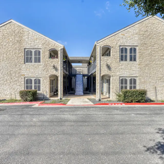 A front view of an apartment complex with stone exterior and wooden accents, featuring two connected buildings and a central walkway.