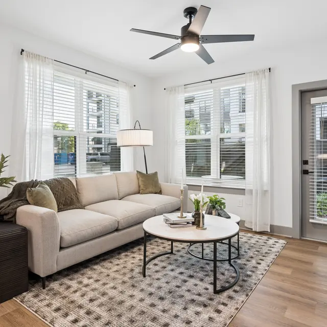 Modern Living Room Interior A cozy living room featuring a beige couch, a round coffee table, and large windows with natural light. A door leads to an outdoor area.