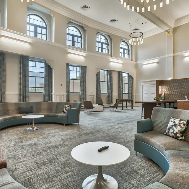 A spacious and modern lobby area featuring curved seating, a round coffee table, large windows, and decorative lighting fixtures.