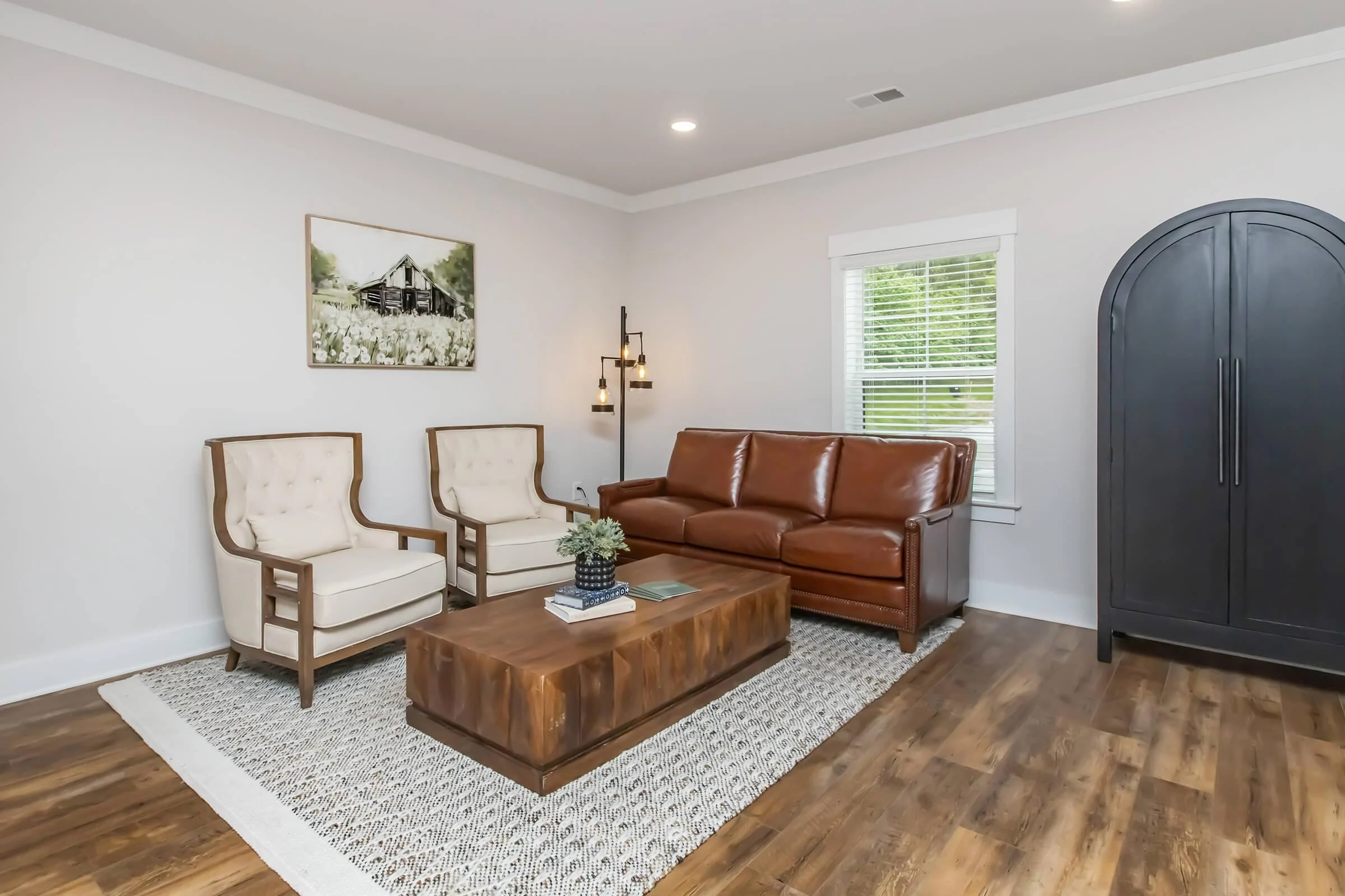 Contemporary Living Room Design A modern living room featuring a brown leather sofa, two cream-colored upholstered chairs, and a wooden coffee table on a patterned rug.