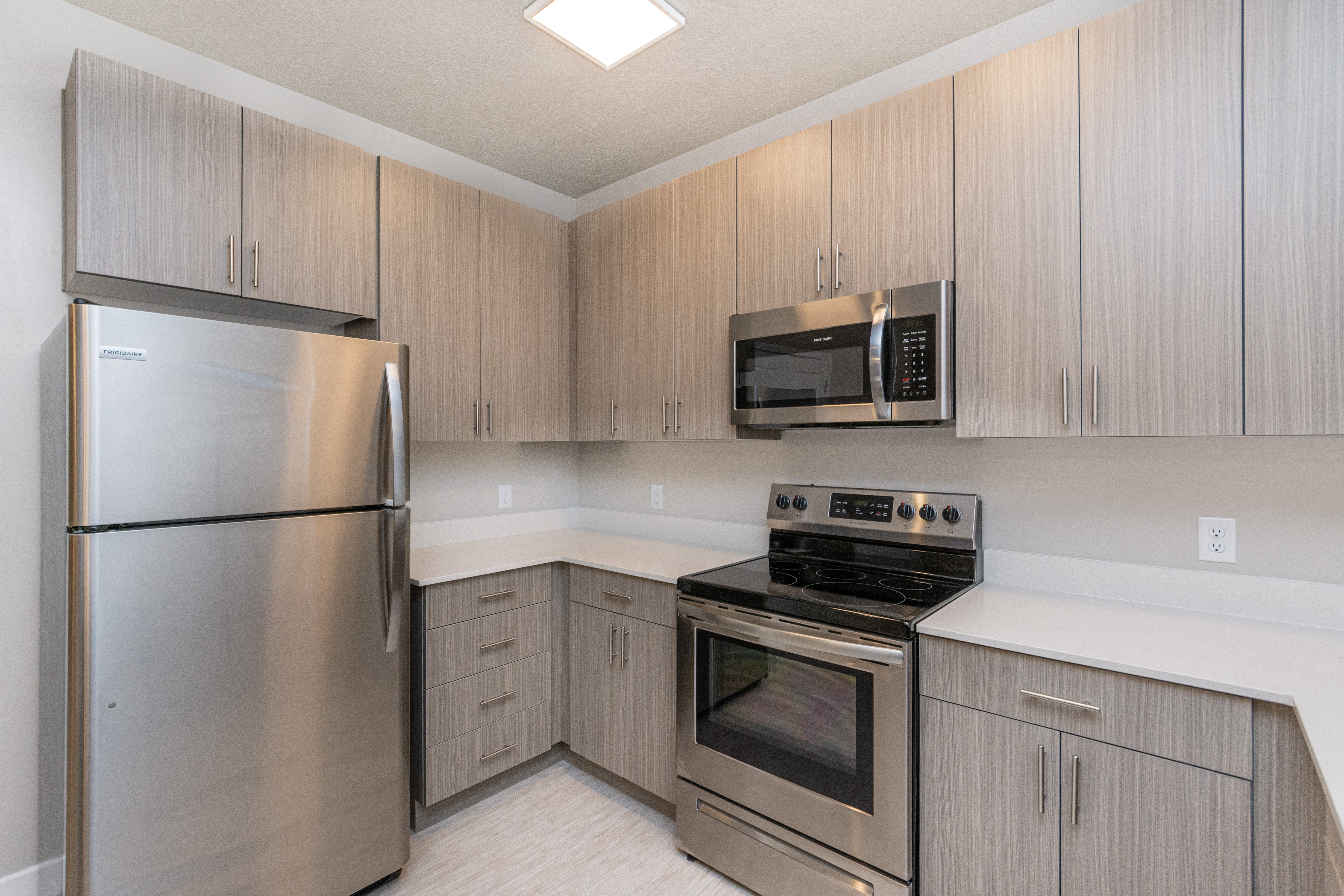 Modern Kitchen Design A modern kitchen with stainless steel appliances, including a refrigerator, stove, and microwave, set against a backdrop of light-colored wooden cabinetry.